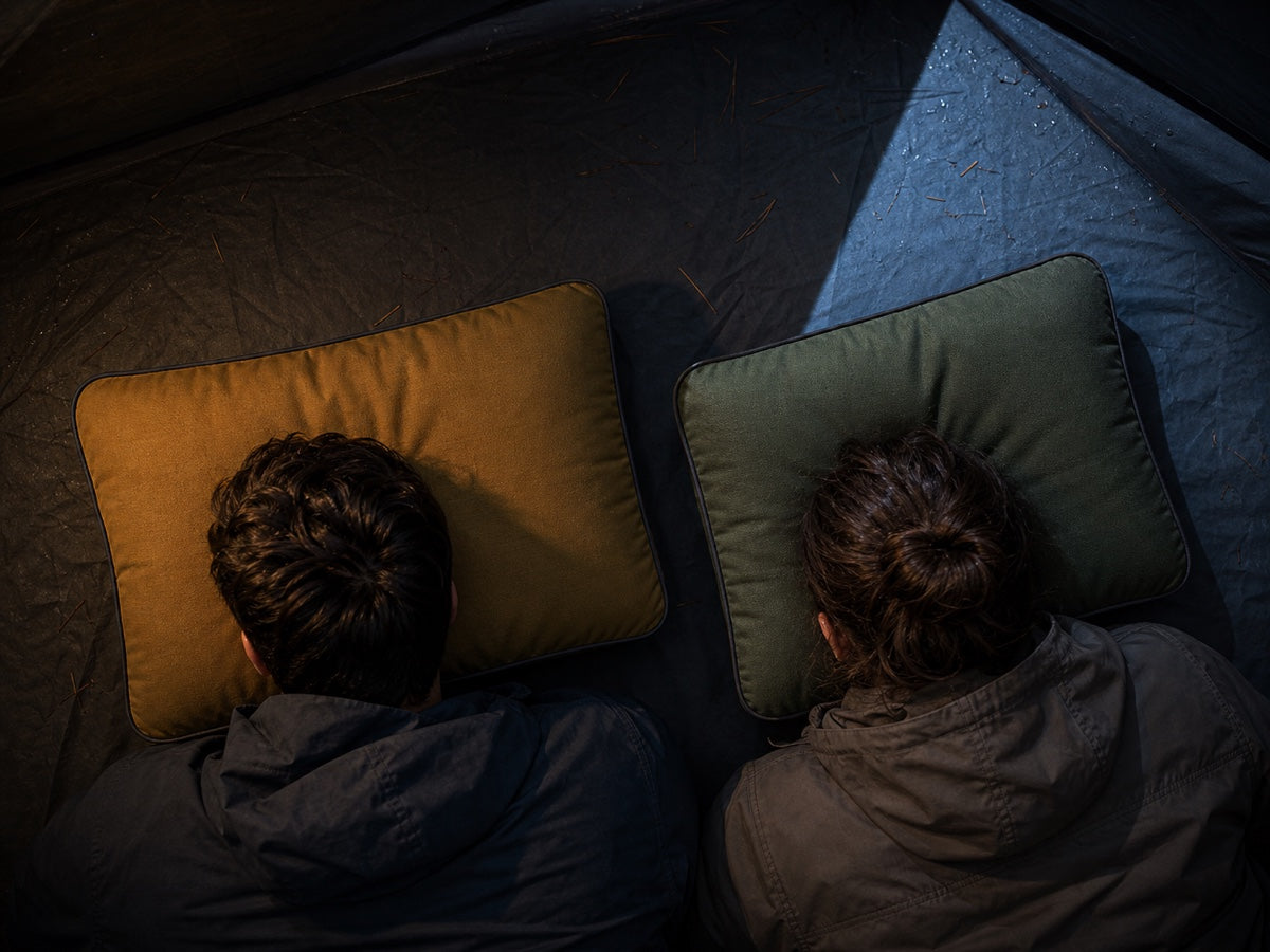Two campers resting on olive and ochre camping pillows